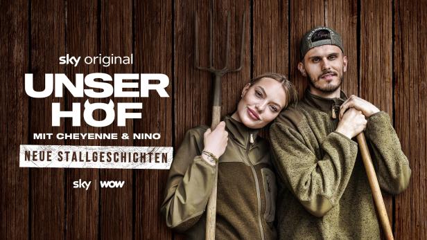 Cheyenne und Nino lehnen mit Mistgabeln an einer Bretterwasnd