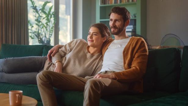 Aneinandergekuscheltes Pärchen daheim auf der Couch beim Streamen