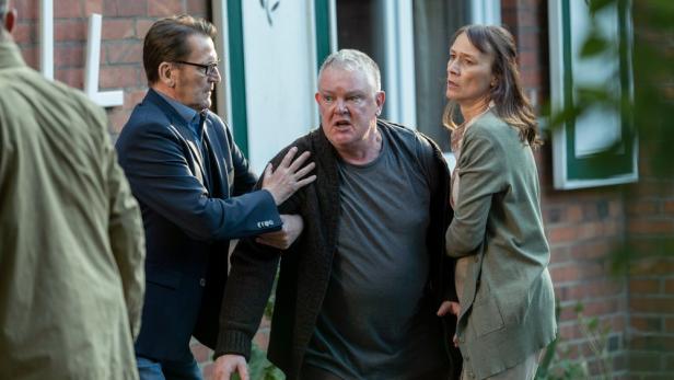 Mann und Frau halten vor einem Haus einen Mann zurück, der auf einen anderen Mann losgehen möchte