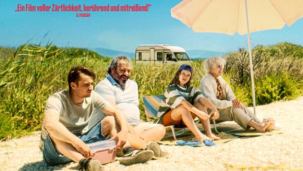 Vier Personen sitzen im Sand - davon zwei Frauen unter einem Sonnenschirm