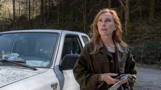 Andrea Sawatzkisteht in Serienrolle neben Auto im Wald