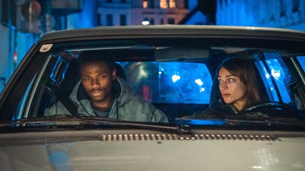 Mann und Frau fahren mit Auto druch eine nächtliche Großstadt