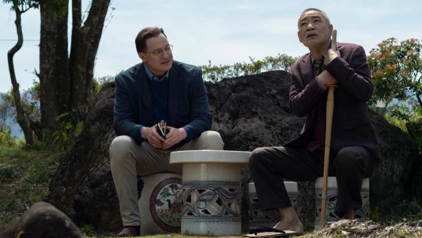 Brendan Fraser sitzt neben japanischem Mann auf Steinbank im Garten