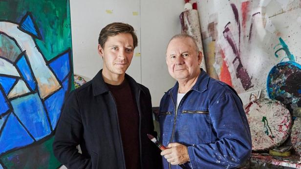 Jüngerer Mann steht neben älterem in dessen Maleratelier