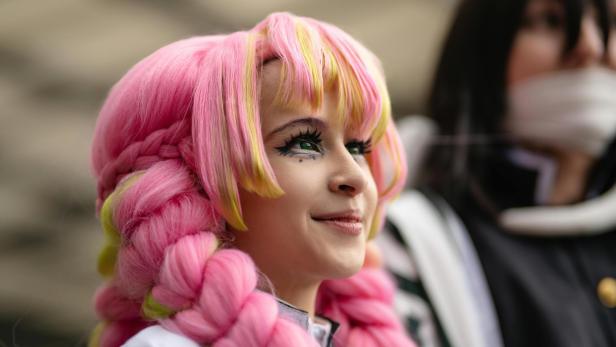 Eine junge Frau mit rosa-gelber Perücke und auffälligem Augen-Make-up lächelt.