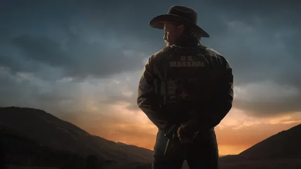 Mann steht in Berglandschaft und hält einen Revolver hinter dem Rücken