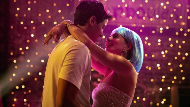 Frau legt vor einer Lichterhintergrund die Arme um den Hals eines Mannes