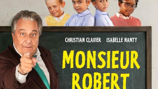 Christian Clavier steht vor einer Schultafel, die den Fimtitel trägt und zeigt mit dem Finger auf uns