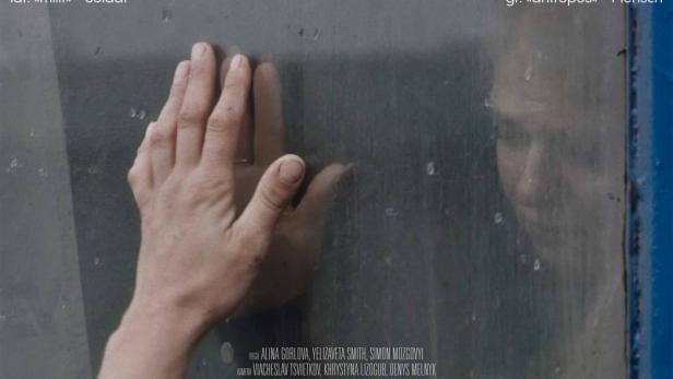 Hand berührt von außen ein Zugfenster, hinter dem eine Frau sitzt