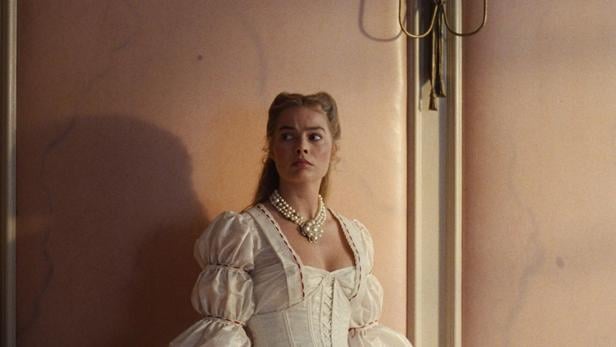 Margot Robbie steht vor einer rosafarbenen Wand