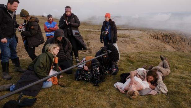 Margot Robbie und Jacob Elordi liegen beim Dreh auf dem Heideboden und sind von der Filcrew umgeben