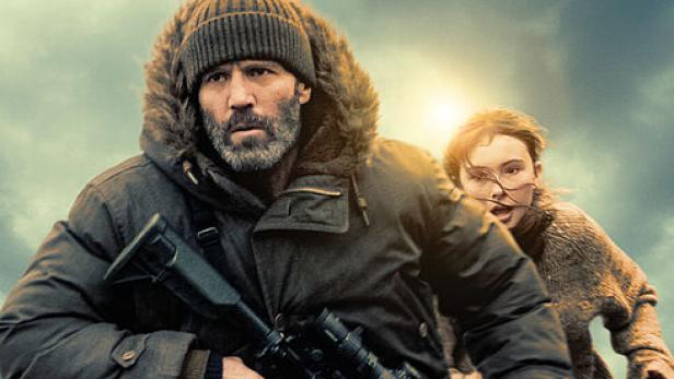 Jason Statham läuft mit einer Waffe in der Hand vor einem Mädchen über einen Strand