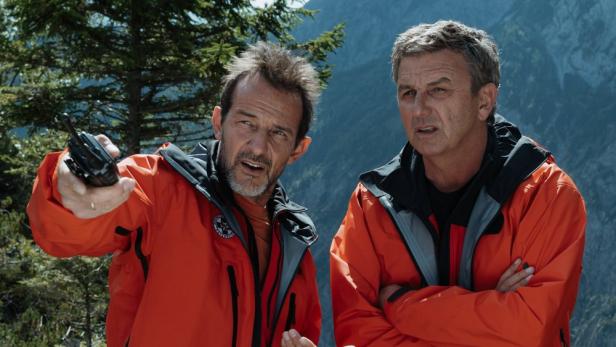 Hans Sigl steht als Bergdoktor mit gekreuzten Armen neben einem Kollegen