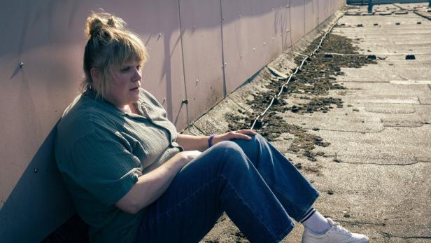 Stefanie Reinsperger lehnt als Ermittlerin Rosa Herzog gegen eine Metallwand gelehnt auf dem Boden