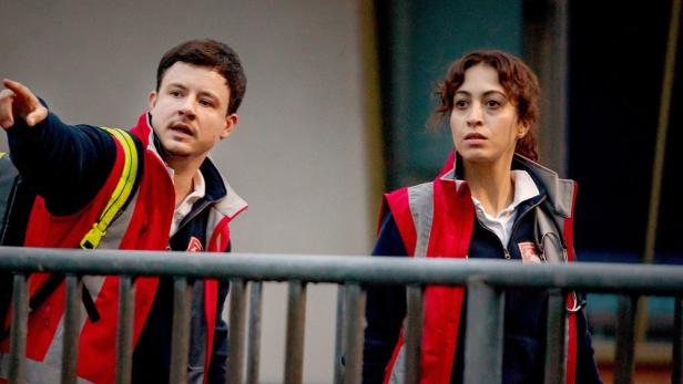 Mann in rotem Sanitäter-Outfit weist seine Kollegin mit dem Finger auf etwas hin