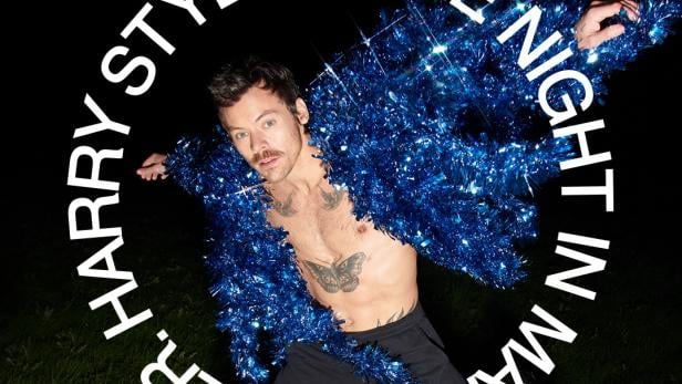 Harry Styles in schrillem Outfit mit ausgestreckten Armen