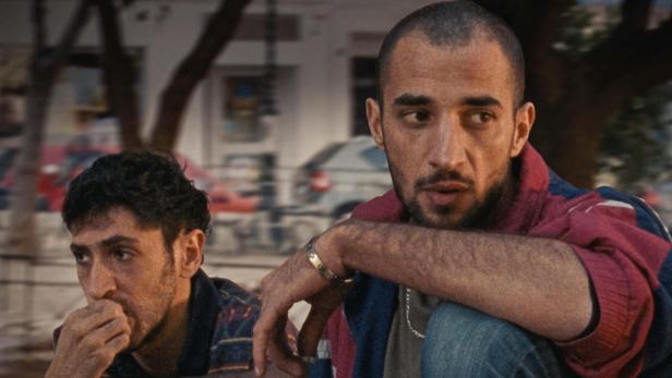 Zwei Männer sitzen auf Filmplakat vor einer Straßenszene