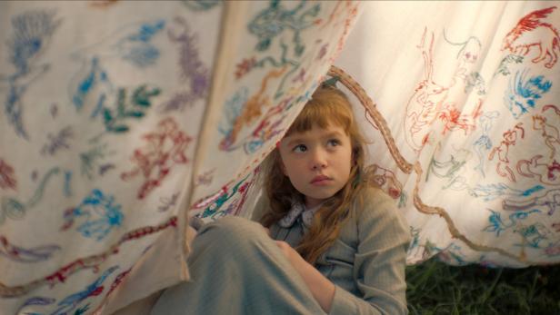 Mädchen sitzt unter einer bunten Decke