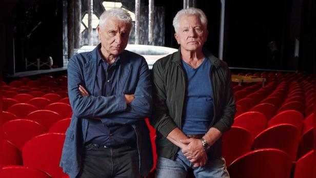 Miroslav Nemec und Udo Wachtveitl in einem Theatersaal an roten Stühlen lehnend