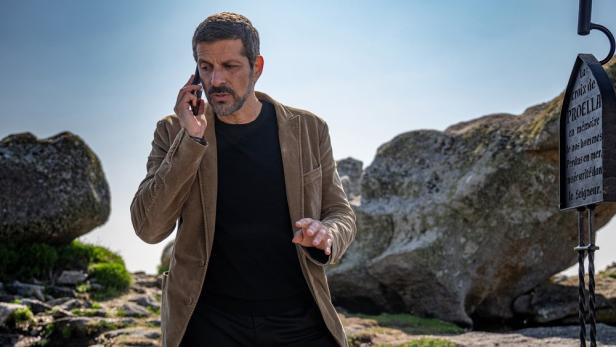 Pasquale Aleardi telefoniert als Kommissar Dupin an der bretonischen Küste vor Felsblöcken