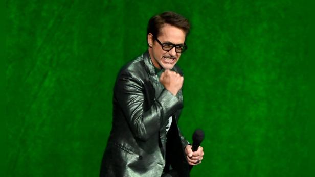 Robert Downey Jr. mit geballter Faust un Mikro in der andern Hand vor grünem Hintergrund