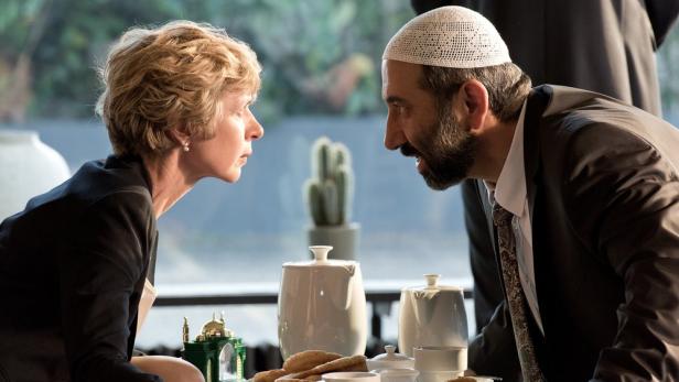 Anna Stieblich als Bürgermeisterin Ursel Piepenkötter und Hilmi Sözer als neuer Hodscha im Gespräch über einen Tisch gebeugt