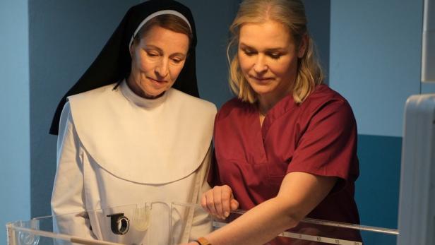 Eine Nonne und eine Hebamme beugen sich über ein Babybett