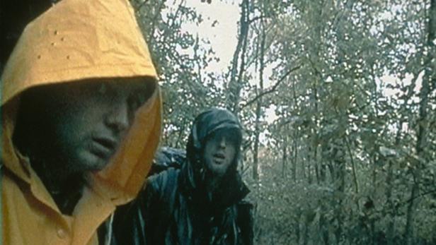 Zwei Männer mit Regenumhängen in einem nassen Wald