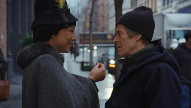 Willem Dafoe und Greta Lee in ihren Filmrollen auf der Straße in ein Gespräch vertieft