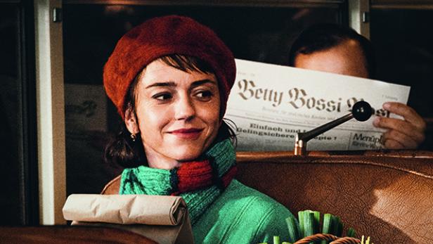 Eine Frau mit Baskenmütze lächelt im Filmplakat zu "Hallo Betty", während ein Mann hinter einer Zeitung hervorlugt.