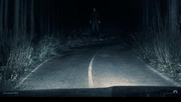 Auf dem Kinoplakat zu "Passenger" steht eine Person auf einer dunklen Waldstraße.