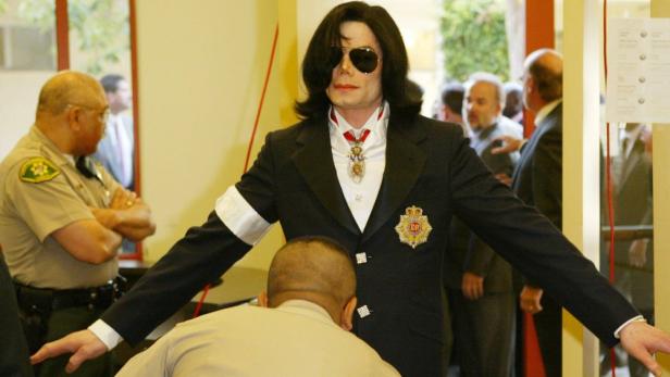 Michael Jackson mit Sonnenbrille und Anzug wird von einem Sicherheitsbeamten am Eingang kontrolliert.