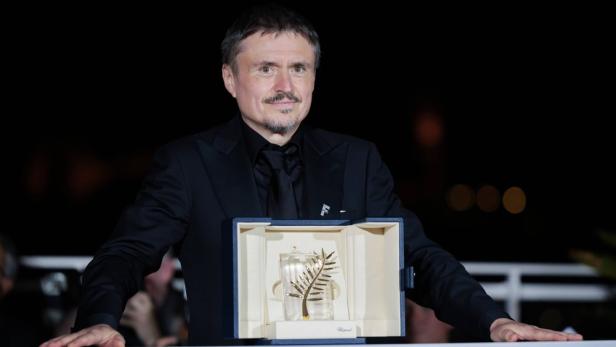 Ein Mann im schwarzen Anzug präsentiert stolz eine Goldene Palme in einer blauen Schatulle.
