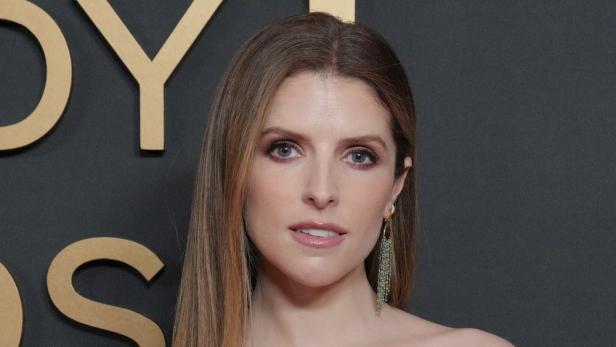 Anna Kendrick mit langem Haar und Ohrring vor dunklem Hintergrund.