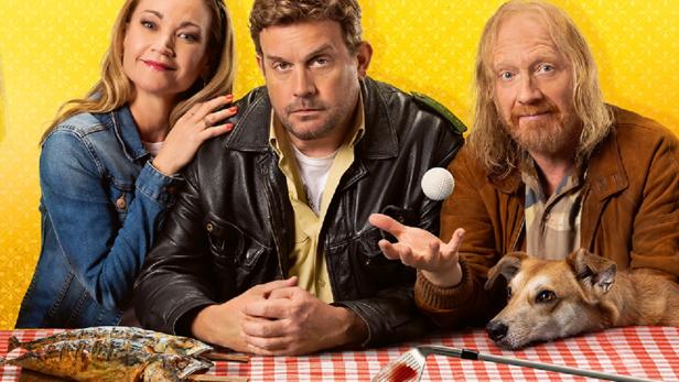Drei Personen und ein Hund sitzen an einem Tisch mit Fisch, blutigem Golfschläger und Ball.