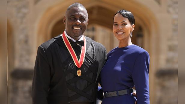 Idris Elba mit umgehängten Ordensband lächelt neben seiner Fau stolz in die Kamera