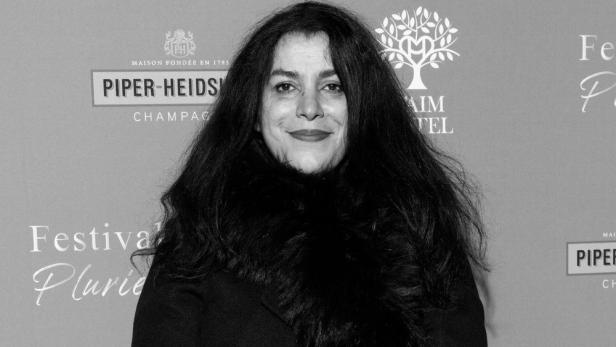 Marjane Satrapi lächelt vor einer Sponsorenwand mit diversen Logos