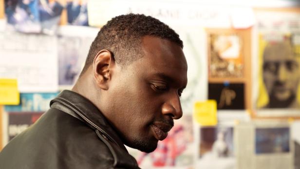 Omar Sy blickt als Lupin nachdenklich vor einer Pinnwand mit verschiedenen Dokumenten und Notizen.