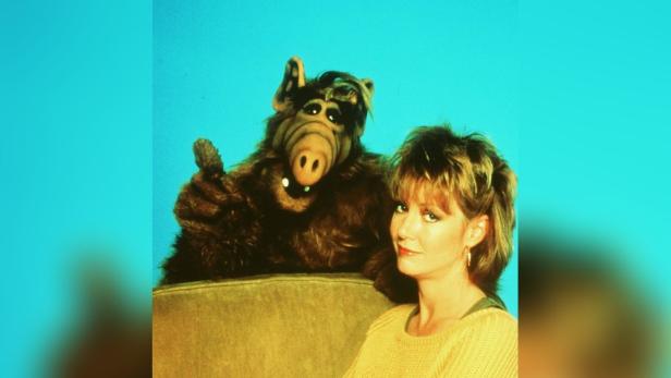 Die Figur ALF und die Schauspielerin Anne Schedeen posieren gemeinsam vor einem hellblauen Hintergrund.
