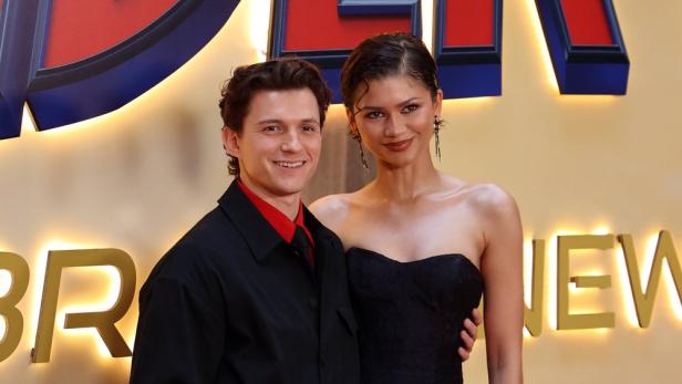 Tom Holland und Zendaya posieren gemeinsam vor einem beleuchteten Hintergrund mit Spider-Man-Schriftzug