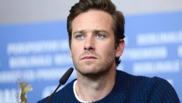 Armie Hammer sitzt vor einem blauen Hintergrund mit Mikrofon bei einer Pressekonferenz.