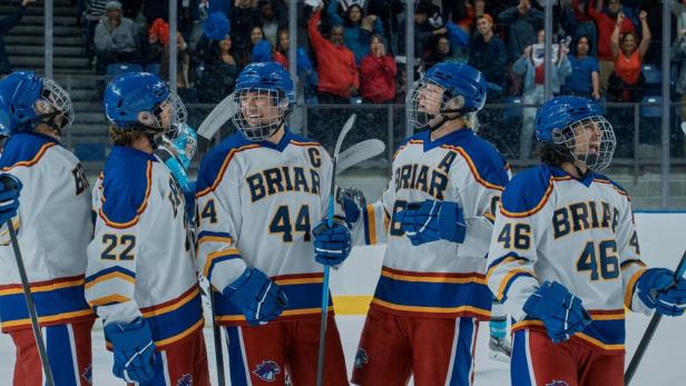 Jubelnde Eishockeyspieler des Briar-Teams in weiß-blau-roten Trikots stehen auf dem Eis vor jubelnden Zuschauern.