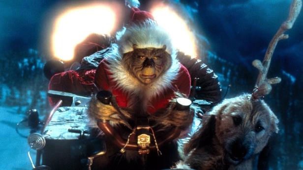 Der Grinch trägt ein Weihnachtsmannkostüm und fährt mit seinem Hund Max auf einem Schlitten durch eine nächtliche Winterlandschaft.