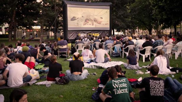 Zuschauer sitzen auf einer Wiese vor einer großen aufblasbaren Leinwand bei einem Open-Air-Kino im Science Park.