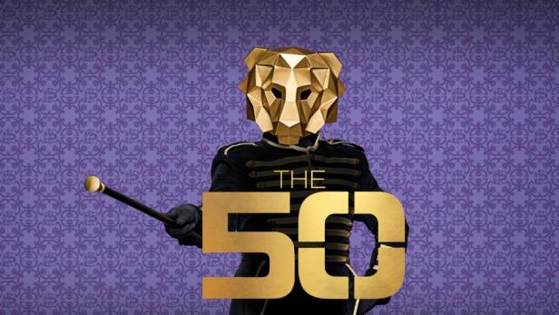 Person mit goldener Löwenmaske und Stock vor violettem Muster, davor der Schriftzug „THE 50“.
