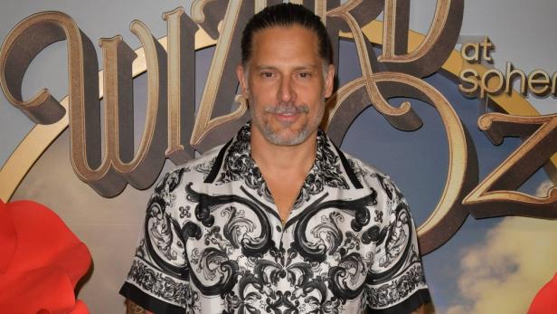 Joe Manganiello trägt ein schwarz-weiß gemustertes Hemd vor einem Hintergrund mit dem Schriftzug „Wizard of Oz“.