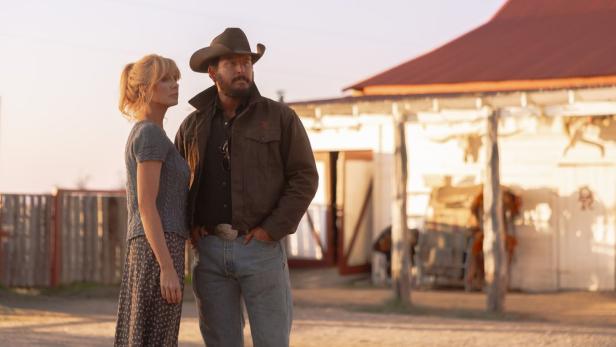 Beth Dutton und Rip Wheeler stehen vor einer Ranch im warmen Licht der Abendsonne.