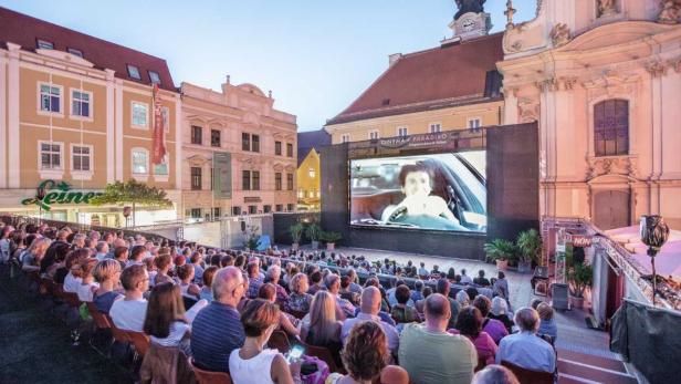 Zuschauer sitzen auf einem Platz vor einer großen Leinwand des Cinema Paradiso in St. Pölten bei einer Open-Air-Filmvorführung.