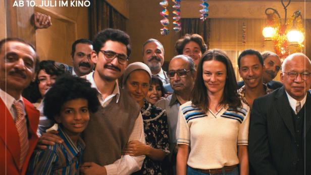 Filmplakat zu „The Stories“ von Abu Bakr Shawky mit Amir El-Masry und Valerie Pachner vor einer Gruppe von Menschen in einem Wohnraum.