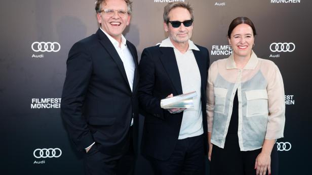 David Duchovny steht mit zwei Personen vor einer Sponsorenwand des Filmfest München.